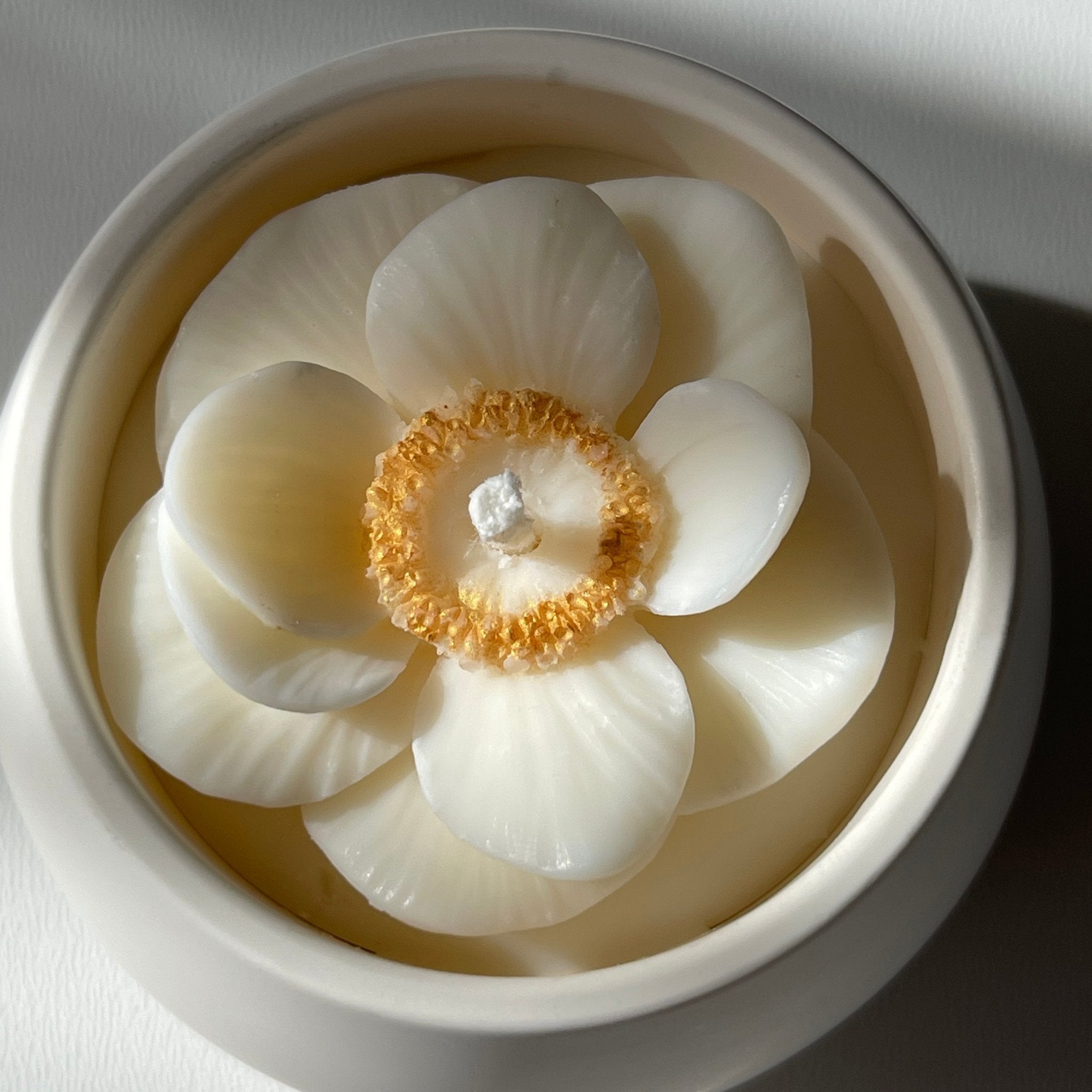 La petite boule blanche "anémone" - bougie parfumée rehaussée d'une fleur anémone coeur doré dans son contenant fait main en jesmonite, vue du dessus