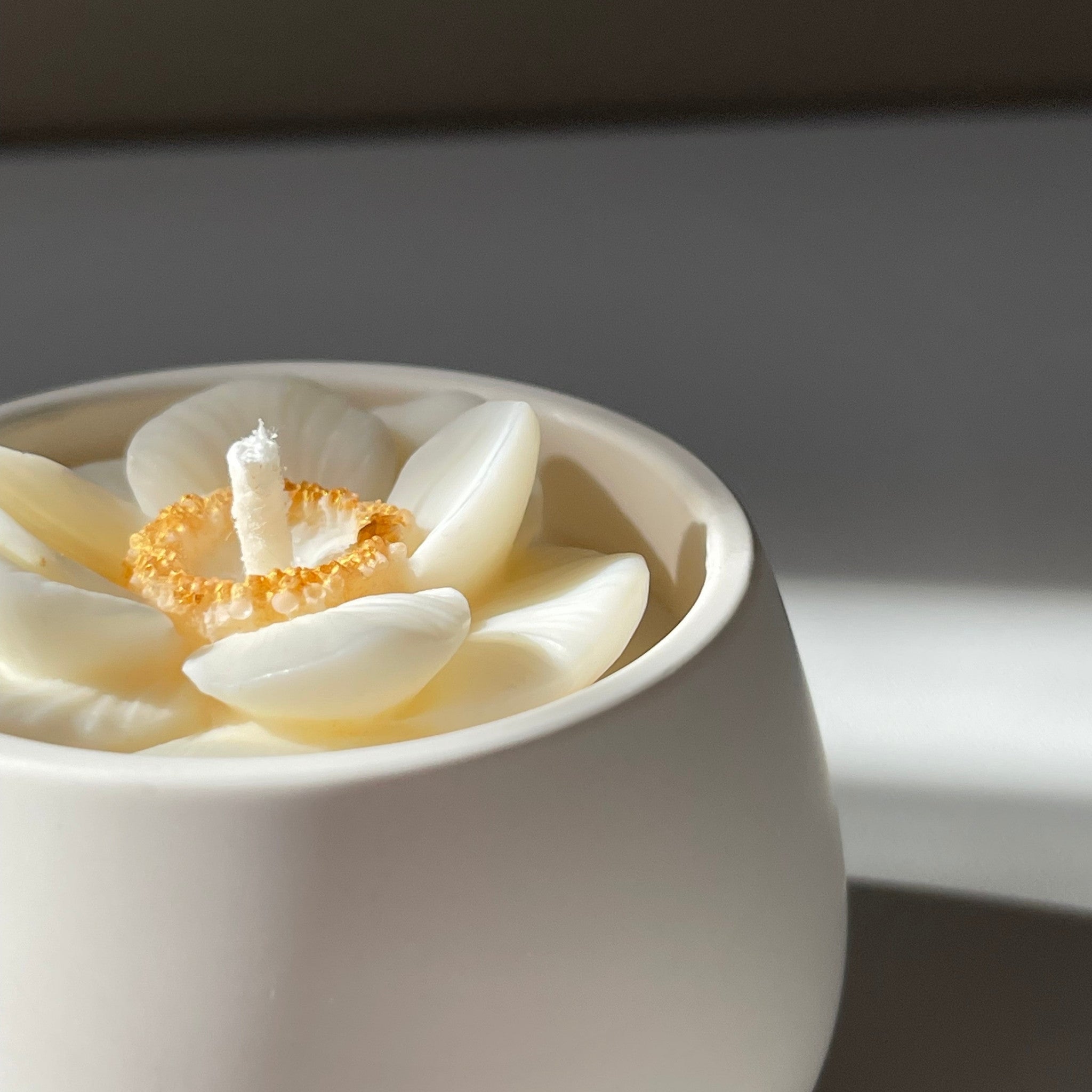 La petite boule blanche "anémone" - bougie parfumée rehaussée d'une fleur anémone coeur doré dans son contenant fait main en jesmonite.
