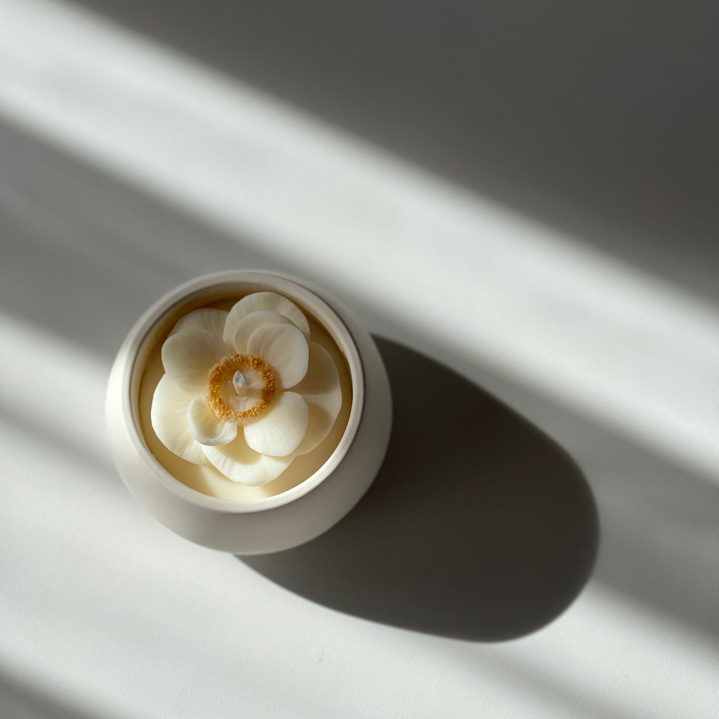 La petite boule blanche "anémone" - bougie parfumée rehaussée d'une fleur anémone coeur doré dans son contenant fait main en jesmonite.