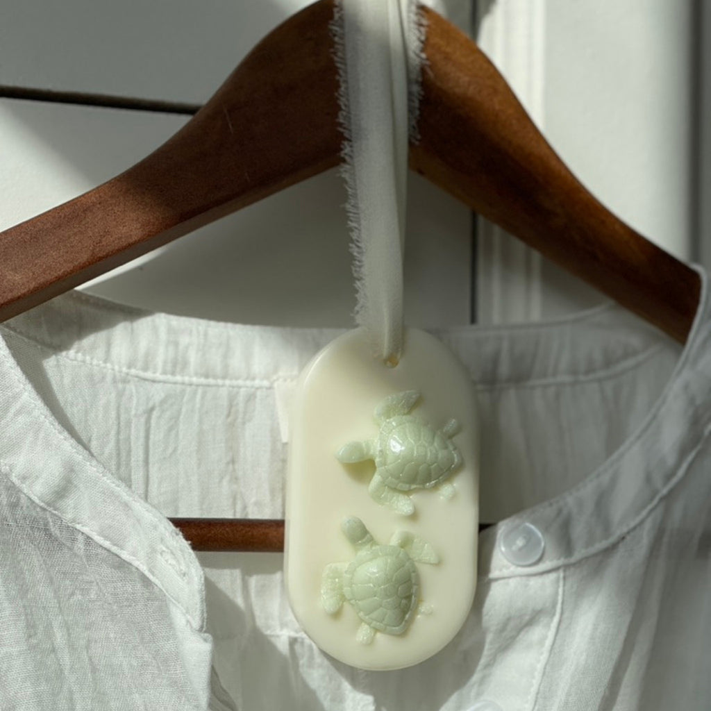 Le coffret cadeau pour les institutrices et puéricultrices - la suspension parfumée bergamote & pamplemousse avec ses deux petites tortues présentée sur un cintre en bois